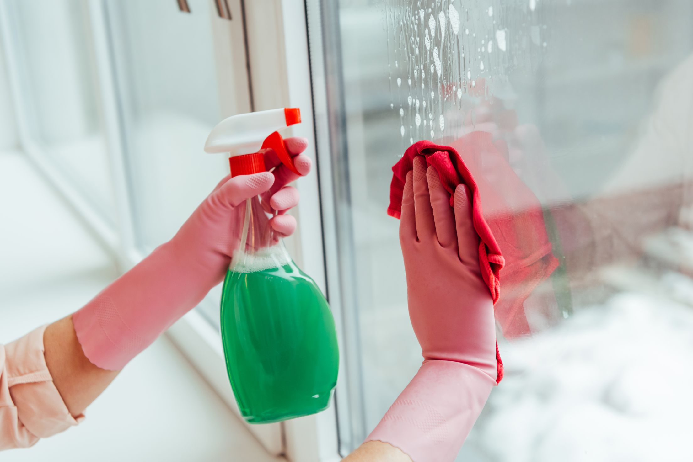 Partial view of woman in pink gloves cleaning window with spray and rag